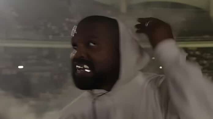Kanye Westが2024年に韓国で行ったライブパフォーマンスの様子。暗闇の中でフードをかぶったKanyeが観客に向かって歩いているシーン。ステージの後ろには観客のライトが輝いており、彼の圧倒的な存在感を際立たせている。ライブの臨場感を伝えるショットで、Kanyeの音楽活動とその影響力を象徴する画像。
