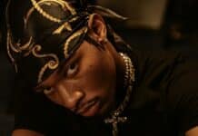 黒いバンダナとジュエリーを身につけたラッパーが床に座り、真剣な眼差しを向けるヒップホップアーティストのポートレート・d4vd