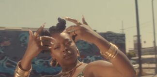 Charm La’Donna:Kendrick Lamar、Beyoncéの振り付けを手がけるストリートダンサーとは? Charm La’Donnaが『Queen』のミュージックビデオで、ロサンゼルスのストリートを背景にハンドサインを掲げる瞬間。金のアクセサリーとエメラルドグリーンのドレスが太陽光に輝き、ヒップホップとアフリカン・フェミニズムの融合を象徴している。