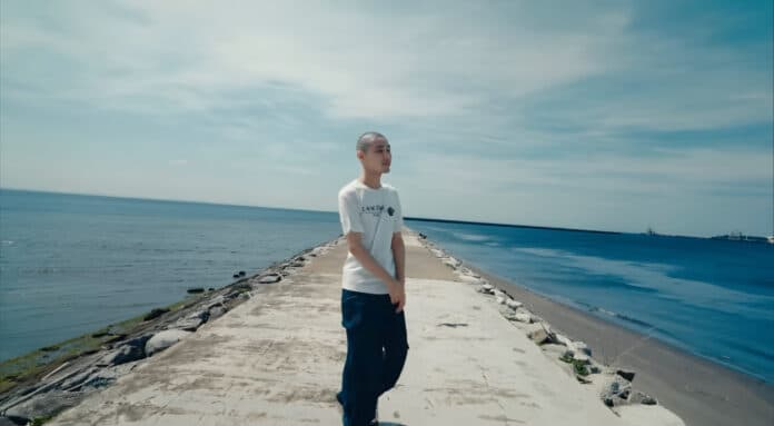 KID FRESINO standing alone on a breakwater by the sea, symbolizing loss and memory in “hikari”