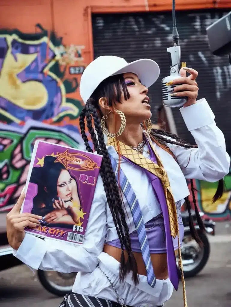 Daimon Yayoi holding a microphone in front of street art, styled like a live-performance visual from a 4SHOOTERS shoot in LA.
