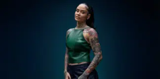 耳を潤す極上のR&Bに浸ろう:Kehlaniの新アルバム『Kehlani』レビュー Kehlaniのポートレート。エメラルドグリーンのレザートップスとネイビースカートを着用し、ミッドナイトブルーの背景の前でポーズを取る。両腕から首元にかけてフルスリーブタトゥー、スリックバックのポニーテール、ゴールドリングを複数着用。HIPHOPCs記事用ビジュアル。