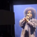 Roots Picnic 2026の会場スクリーンに映る、アフロとサングラス姿でマイクを握りフリースタイルを披露するJay-Z