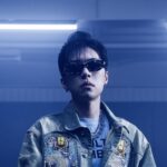 デニムジャケットにサングラス姿で青い照明の中に立つラッパーCityBabyのアーティスト写真