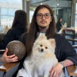 サロンの椅子に座り、白い犬を膝に抱くヘアアーティストのBraidKingNori