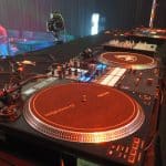 赤い照明に照らされた2台のターンテーブルとミキサーが並ぶDMC Middle EastのDJブース