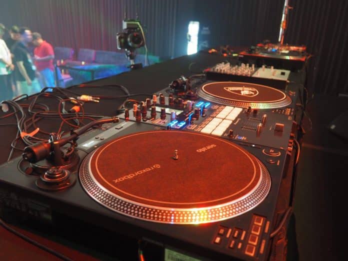 赤い照明に照らされた2台のターンテーブルとミキサーが並ぶDMC Middle EastのDJブース