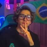 dominguap wearing glasses and a cap in a colorful room with a Brazilian flag behind him