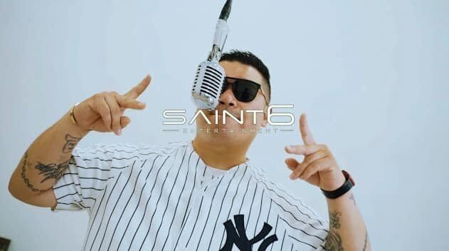 Rapper R-Naby in New York Yankees pinstripes standing at a vintage microphone in the ‘Hey New York’ music video