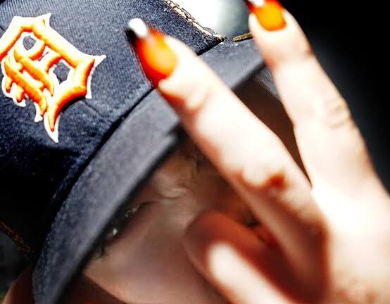 Close-up of SEDY NEZZ in a dark cap, holding two fingers with flame-pattern nails near the camera