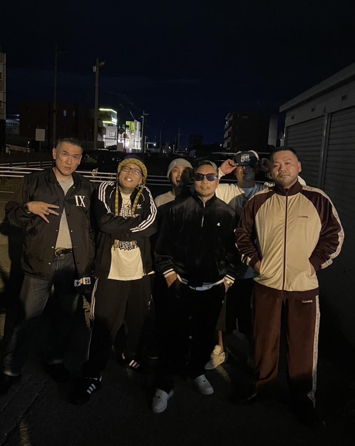 夜の屋外で5人のアーティスト仲間と並ぶ田中雄士