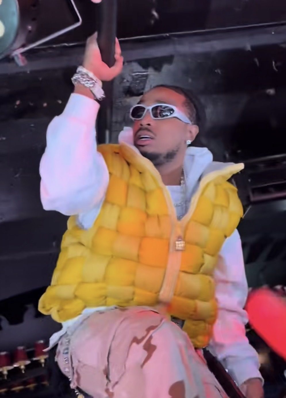 黄色いベストと白いパーカー姿で、ステージ付近の構造物につかまるQuavo。