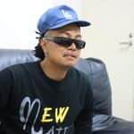 青いLAキャップと黒いサングラスを着用し、ソファに座るMAIKI BOOGIE